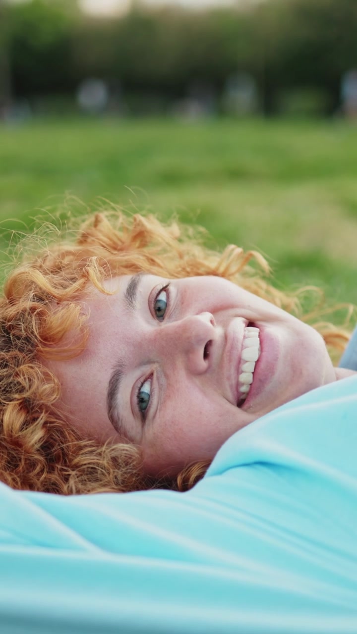 Donna dai capelli rossi gioiosa che si rilassa sull'erba verde nel parco