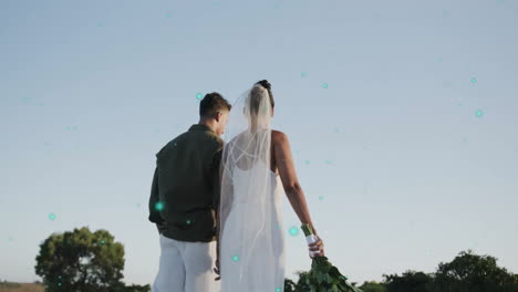 bride and groom walking outdoors with glowing particles animation over sky