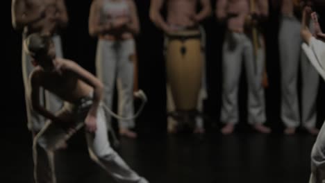 group of a professional dancers are practicing capoeira in darkness against a spotlight on a black background of studio. afro-brazilian martial art that combine elements of dance.