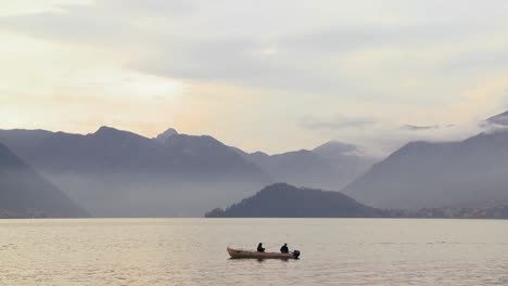 two fishermen fish from a boat on a beautiful lake in front of the italian alps 2