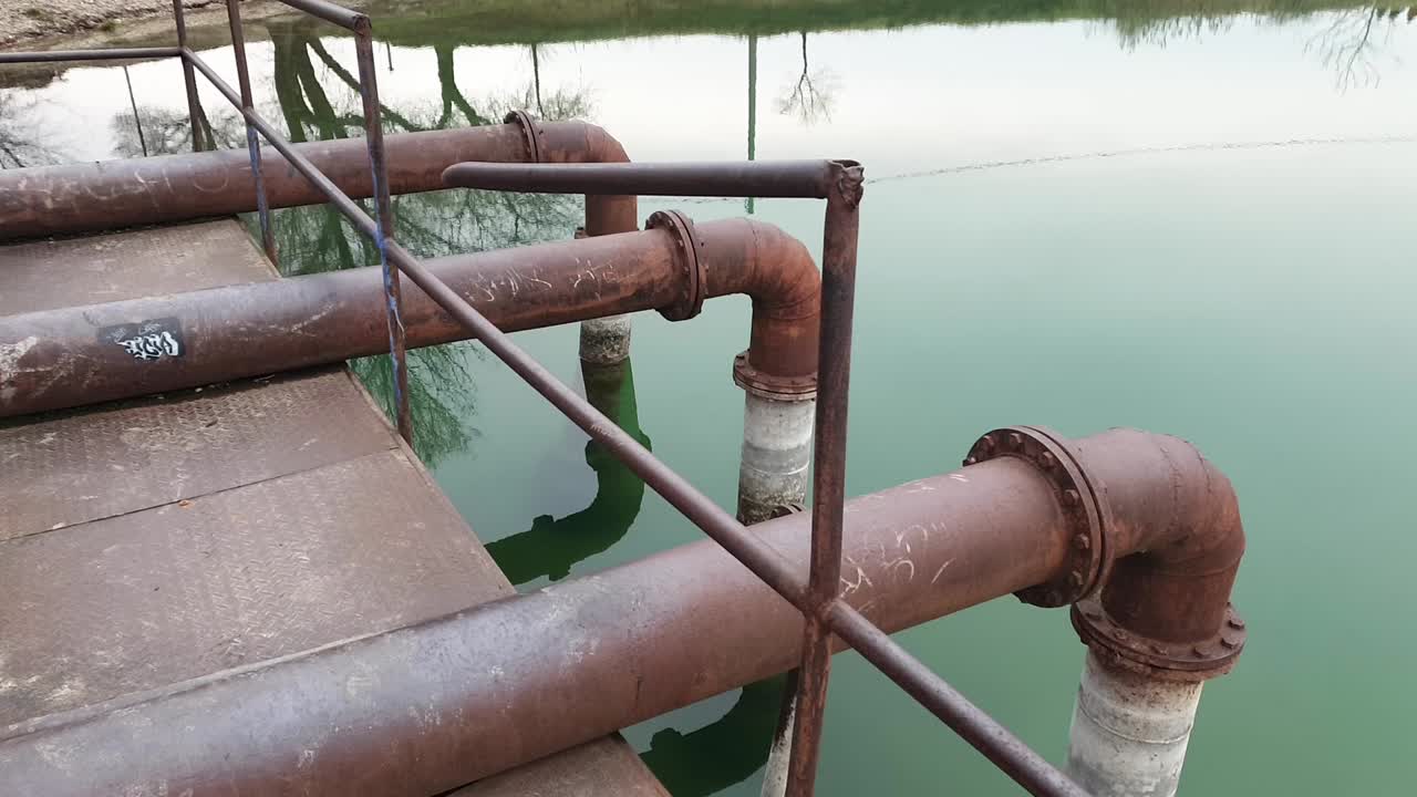 muelle de bombeo de agua abandonado y oxidado en un cuerpo de agua verde