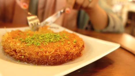 a person eating kunefe with pistachio and syrup