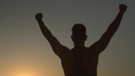 Muscular-man-stranding-on-seashore-at-sunset