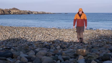 Einsamer-Mann-In-Warmer-Kleidung-Geht-Am-Felsigen-Morgenstrand-Auf-Die-Kamera-Zu