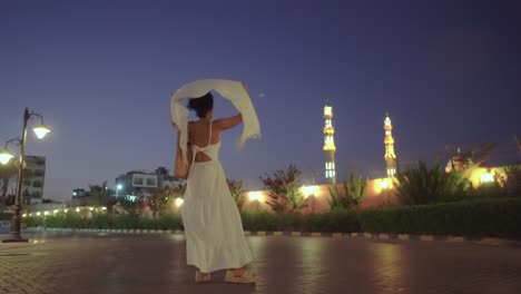 evening view of el mina mosque with lights and tourist woman in long white dress and white scarf waving on the wind in hurghada, egypt