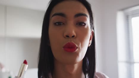 Mixed-race-gender-fluid-person-standing-in-bathroom-and-using-a-lipstick
