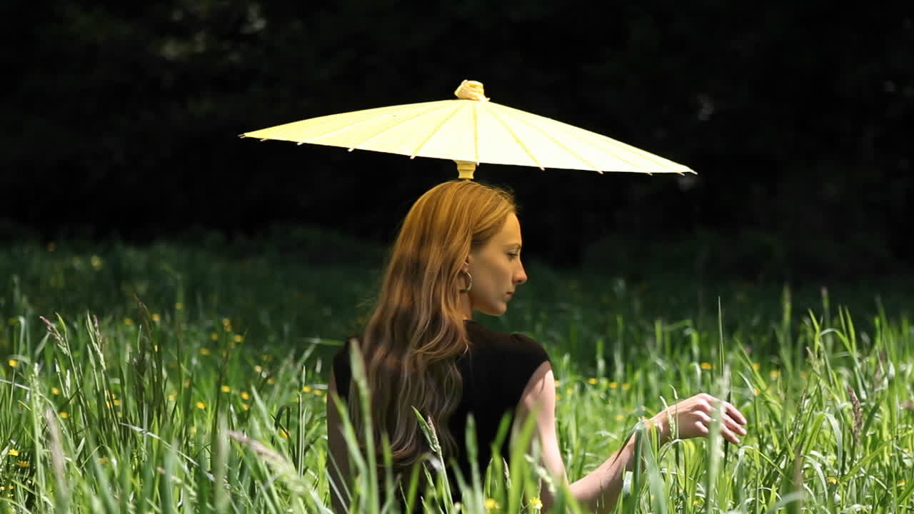 한 여성이 땅에 앉아 풀잎을 섬세하게 애무하고 있습니다.