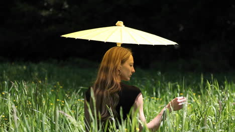 a woman sits on the ground delicately caressing a blade of grass