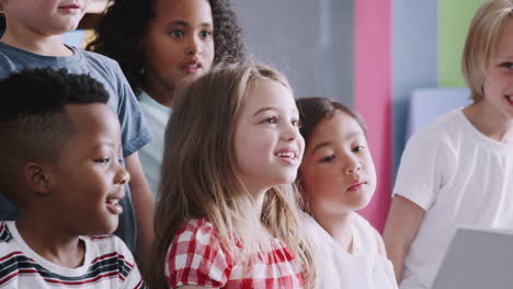 elementary pupils raising hands to answer question as female teacher reads story in classroom