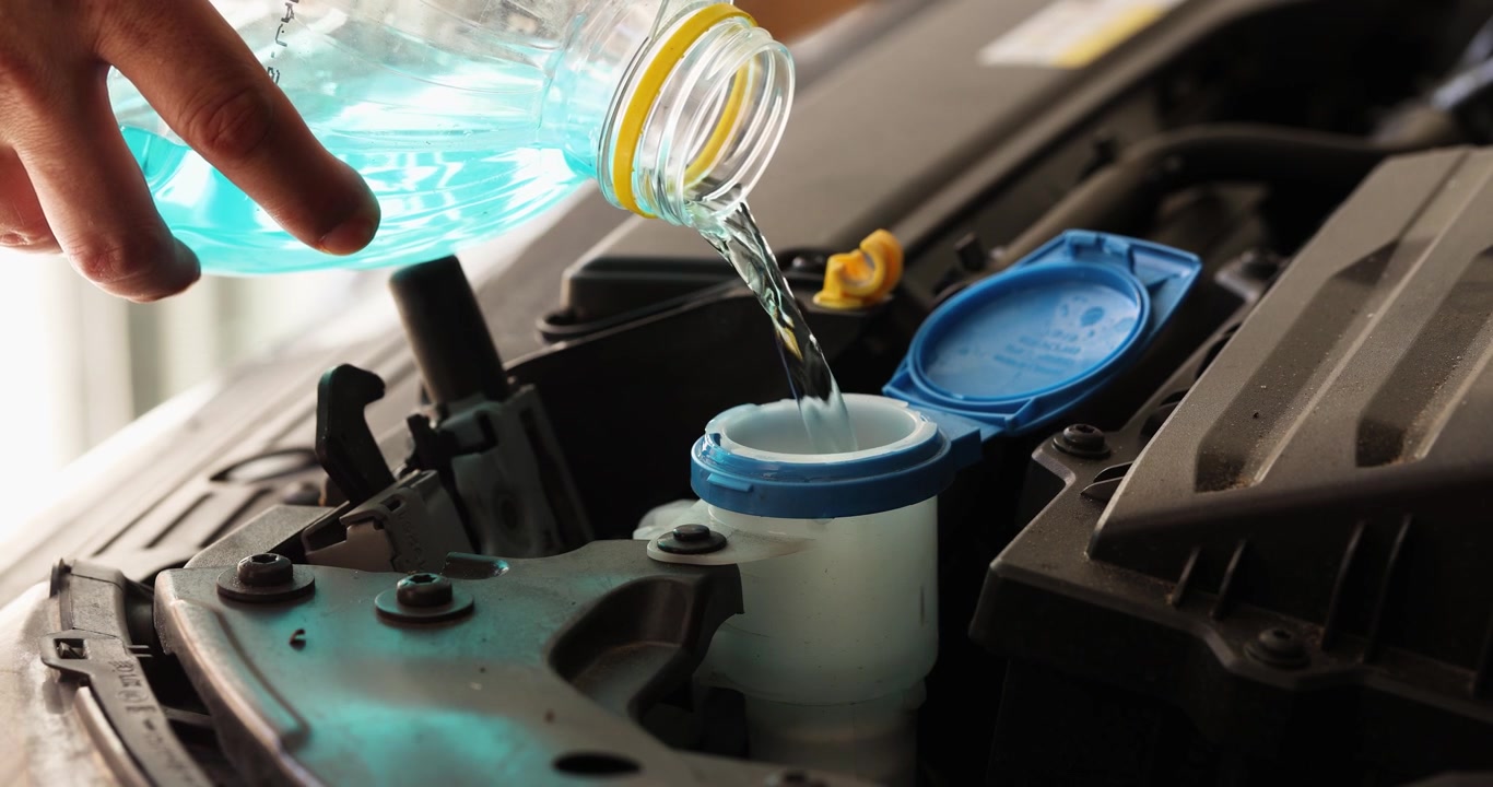 Close-up shot of driver or car owner pours blue windshield washer fluid into a car reservoir under the hood.