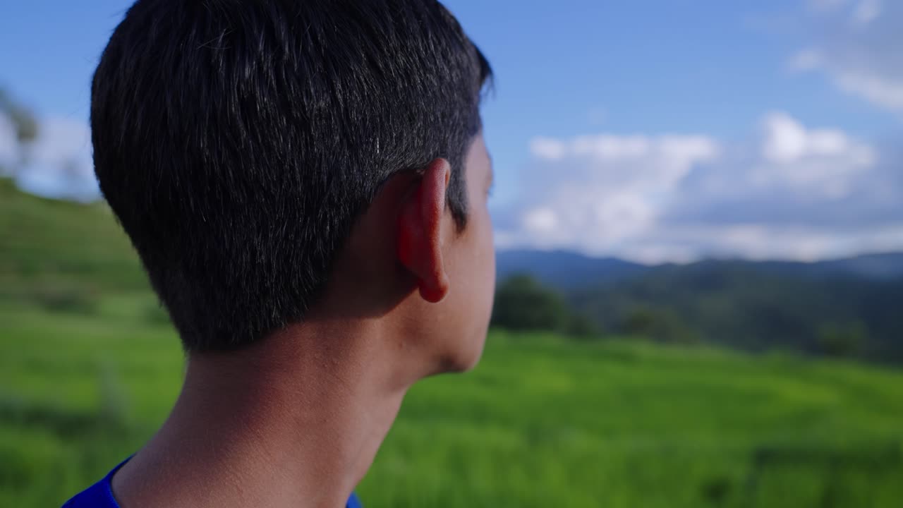 Close-up of nervous young boy in rice field glancing around, unsure expression in rural setting, 4k video