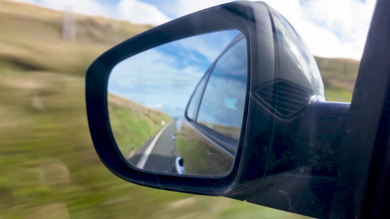 Lo specchietto retrovisore laterale cattura una strada tortuosa e un paesaggio in rapido movimento, evocando velocità e concentrazione