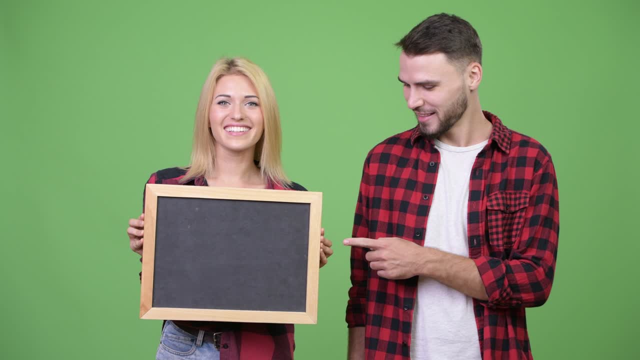 Young couple holding blackboard and pointing finger together