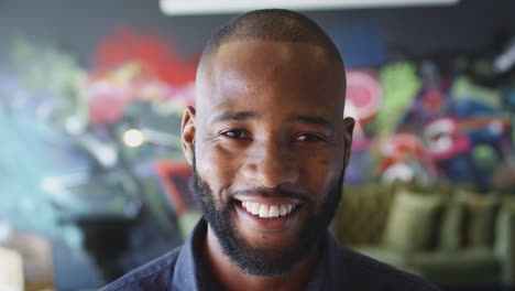 millennial black man smiling to camera in front of mural in workplace, head shot