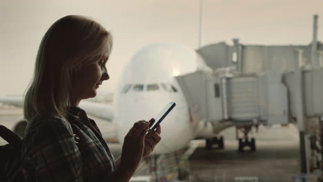 mujer viajera usa un teléfono inteligente en la terminal del aeropuerto en el fondo de un gran avión fuera