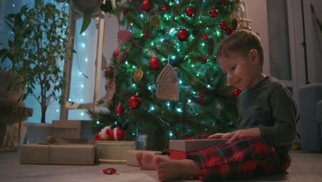 the boy opens the gift and the light from the box illuminates the joyful face. open a gift under the tree. high quality 4k footage