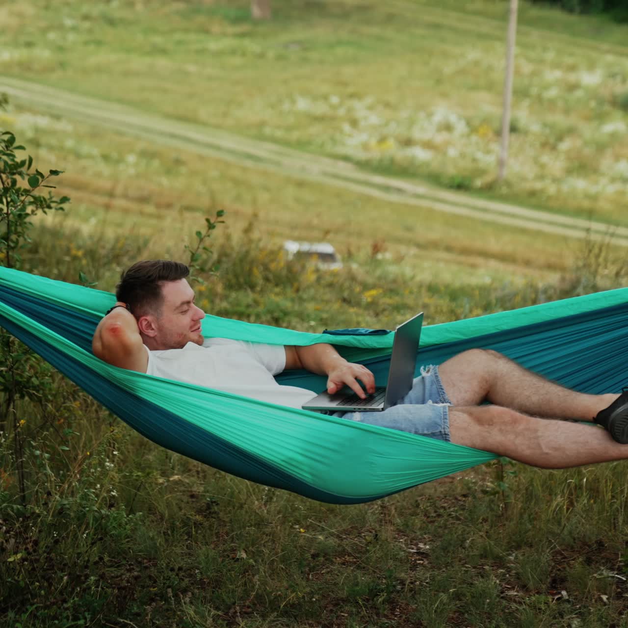 Caucasian man lies in the hammock. Relaxed freelancer works on laptop remote from the office