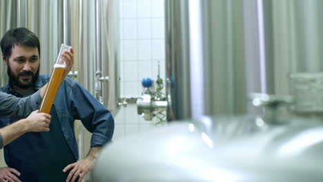 coworkers smiling, looking at freshly brewed unfiltered beer in glass and discussing it at brewery