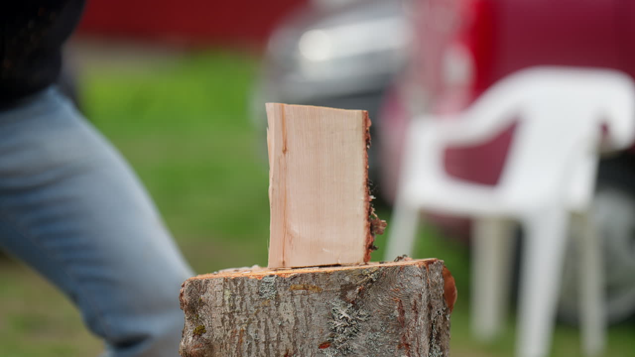 Man lands powerful axe chop slicing wood cleanly in half on block, open grassy farm blurred backdrop
