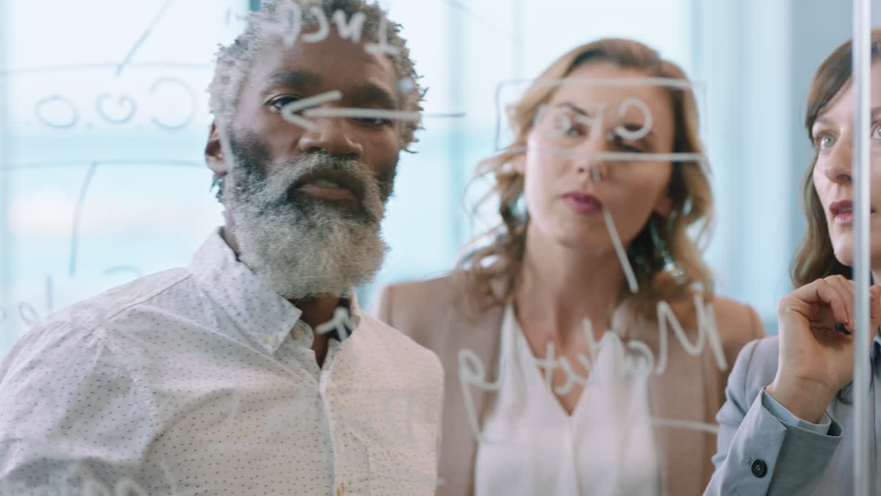 gente de negocios usando notas adhesivas en pizarra de vidrio líder de equipo maduro hombre brainstorming con colegas trabajando en una solución discutiendo la estrategia para el proyecto fecha límite en la reunión de gestión de la oficina