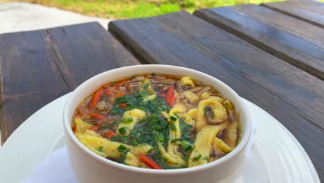 Traditional-Austrian-Frittatensuppe-with-a-stunning-summertime-mountain-view-in-Tyrol-Austria,-delicious-hot-comforting-soup-in-Serfaus-Fiss-Ladis,-4K-shot