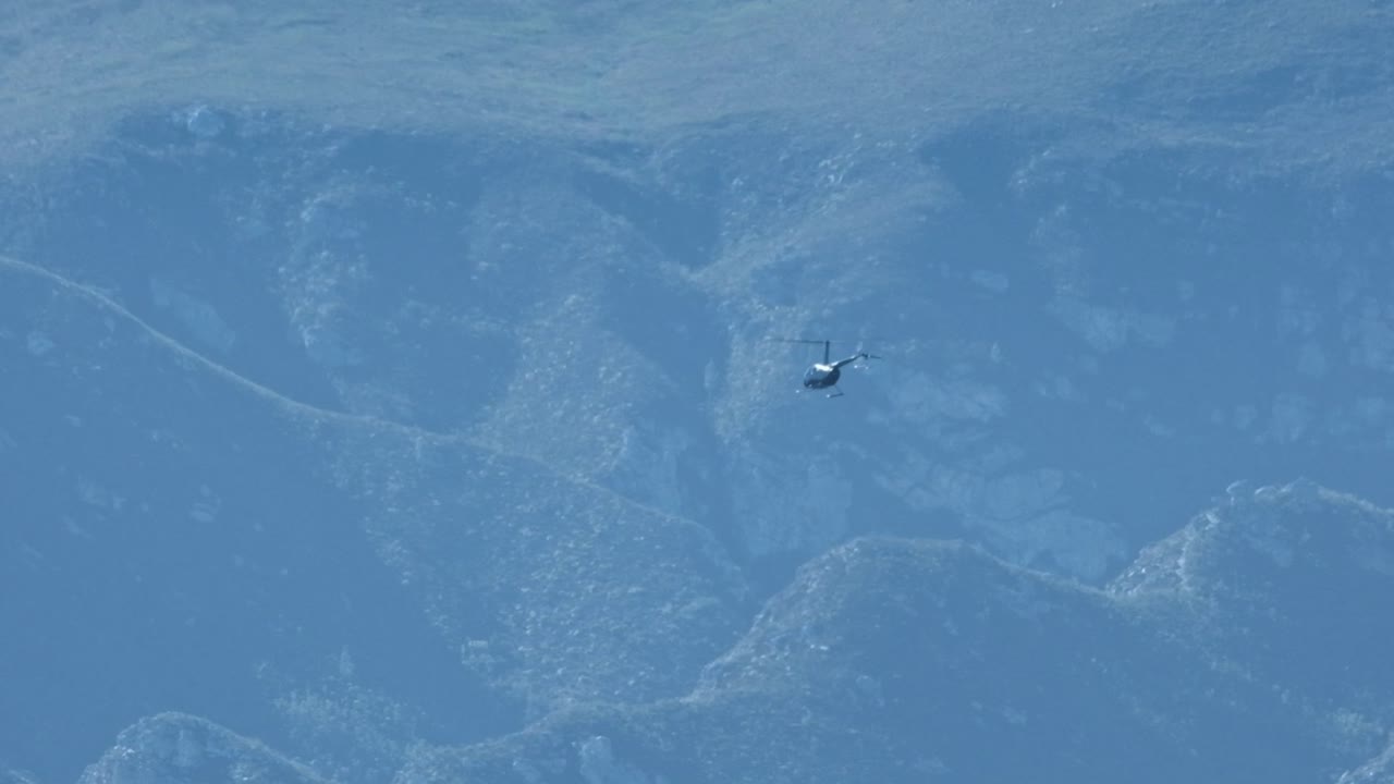 A chopper flies with a spectacular mountain range in the distance