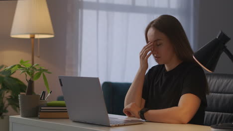 Una-Mujer-Cansada-Está-Trabajando-Con-Una-PC-En-Casa-Por-La-Noche-Sintiendo-Dolor-De-Cabeza-Frotándose-Las-Sienes-Para-Aliviar-La-Tensión-Y-El-Dolor-Trabajando-Demasiado-Después-De-La-Oficina