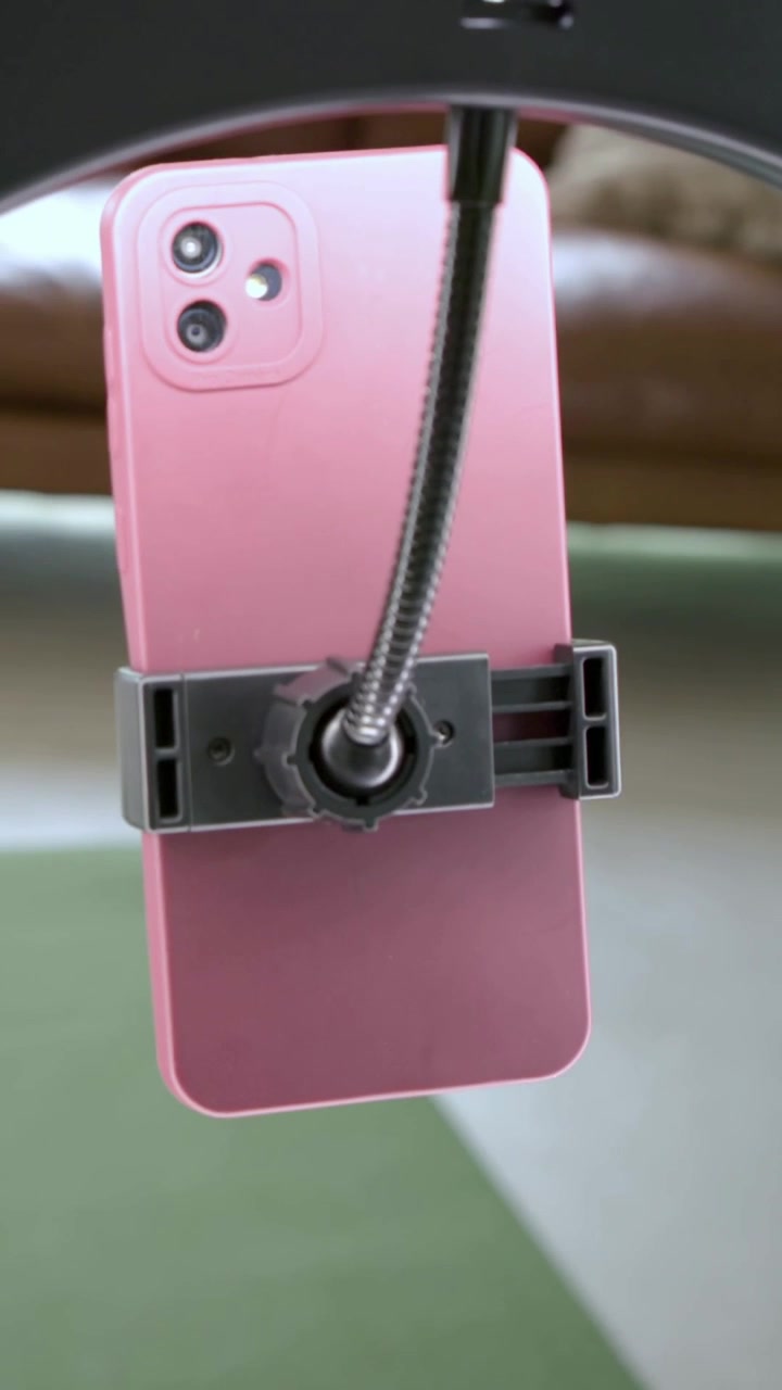Video verticale: Morsetto che si abbassa, tenendo un telefono rosa sotto un anello per registrazioni casalinghe, stringendo la manopola.