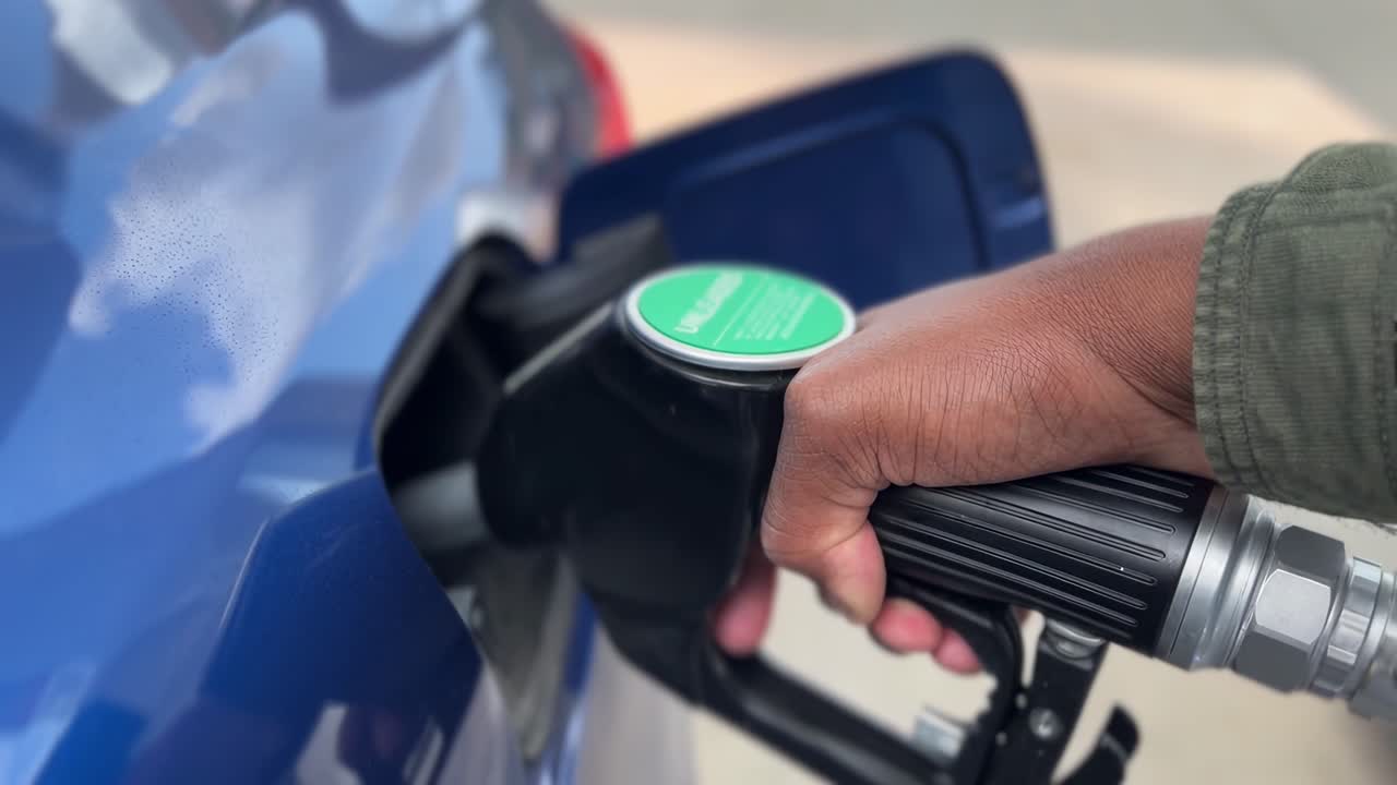Inquadratura video ravvicinata di una mano che fa rifornimento a un'auto blu, evidenziando il carburante ecologico.