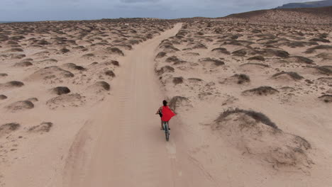 drone following a young girl on the cycle rides on a white sand road