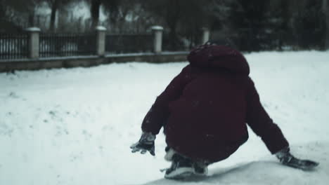 niño sube una colina nevada y se desliza hacia abajo en la espalda, cámara lenta de mano