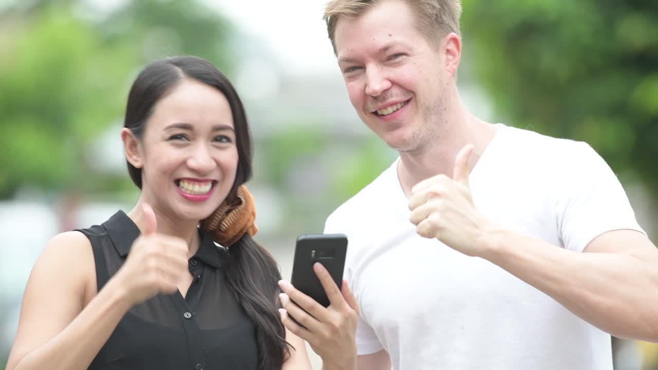 Young multi-ethnic couple using phone together in the streets outdoors