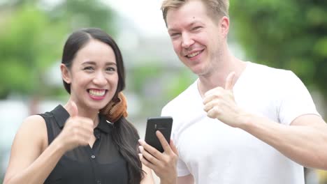 young multi-ethnic couple using phone together in the streets outdoors