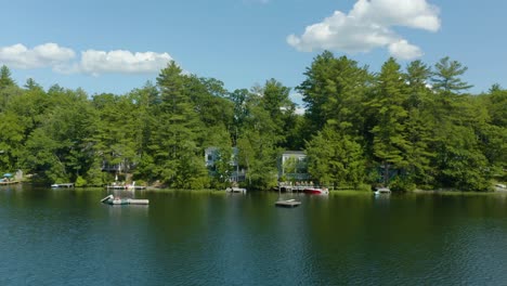 aerial drone backward moving shot of posh lakeside wooden houses along the sunset lake in new hampshire on a bright summer day