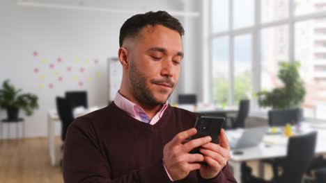 Primer-Plano-De-Un-Hombre-De-Negocios-En-Una-Oficina-Abierta-Moderna-Mirando-Y-Usando-Un-Teléfono-Móvil