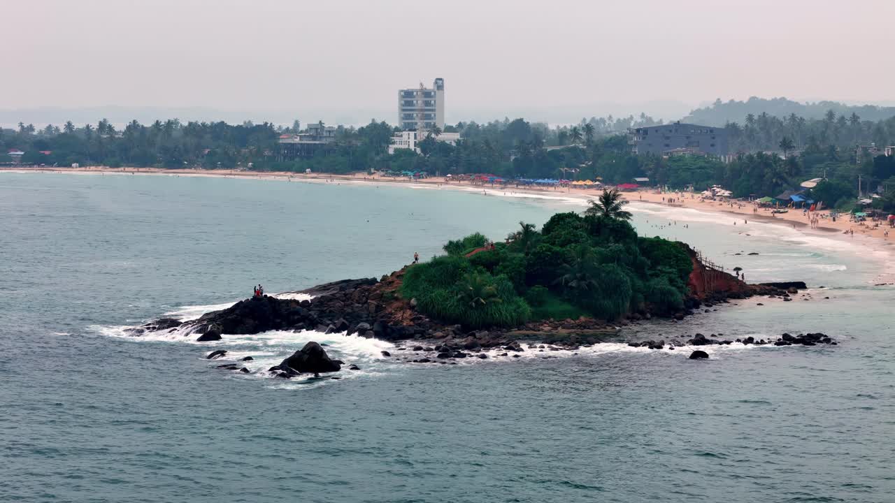 Mirissa Sri Lanka High-angle telephoto reveals details of Parrot Rock, on a hazy day Visitors explore the islet, contrasting the pale beach town backdrop