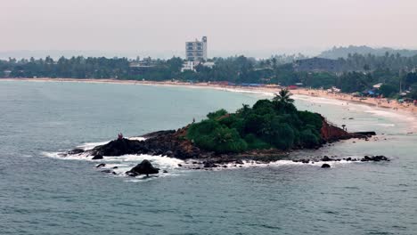 mirissa sri lanka high-angle telephoto reveals details of parrot rock, on a hazy day visitors explore the islet, contrasting the pale beach town backdrop