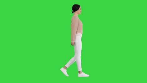 relaxed young woman walking towards and looking with smile at camera in casual style clothes on a green screen, chroma key