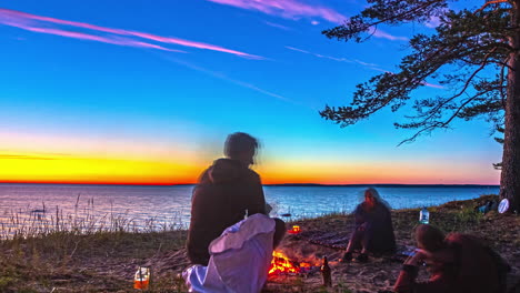 friends enjoying a campfire at a vibrant sunset over the lake