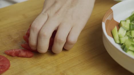 chef cuts tomatoes with kitchen knife on wooden cut board