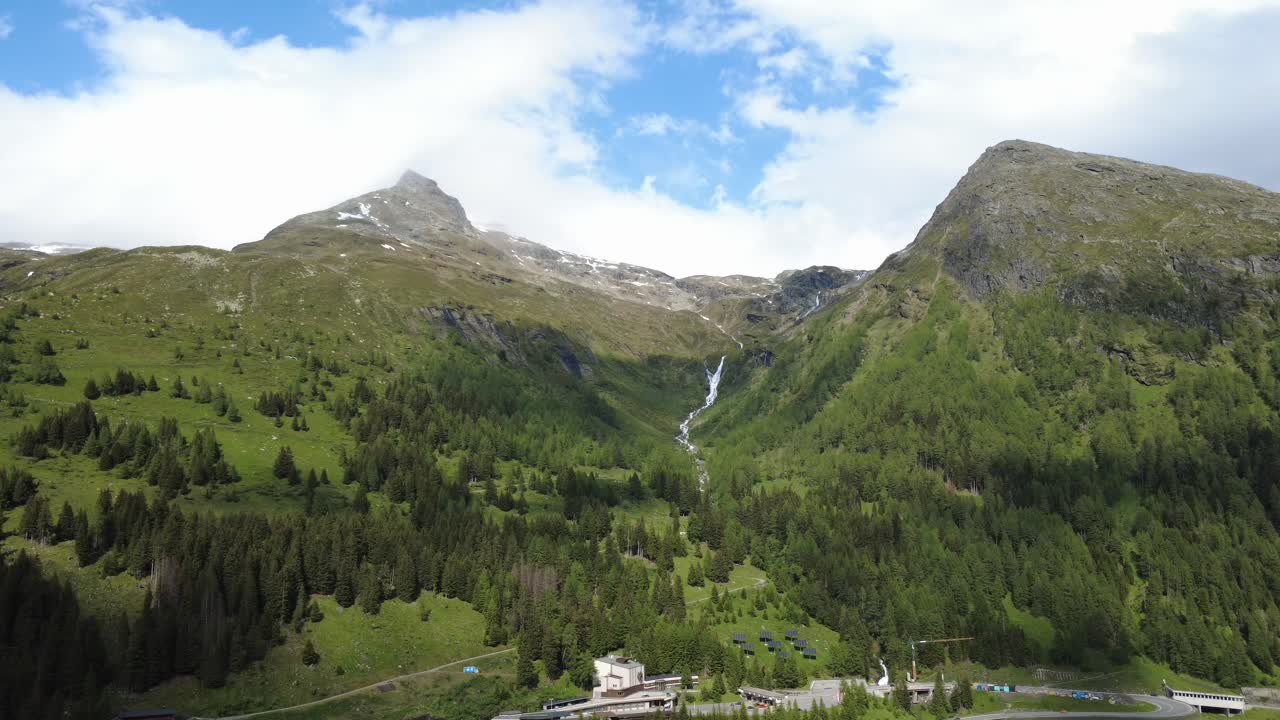 Aerial shot of alpine valley with waterfall and remote building infrastructure.