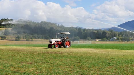 red tractor actively spraying water across a field