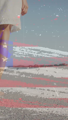 animation of american flag over african american woman walking at beach