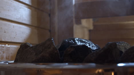 Water-pouring-over-steamy-sauna-stove-in-Finland,-close-up-shot