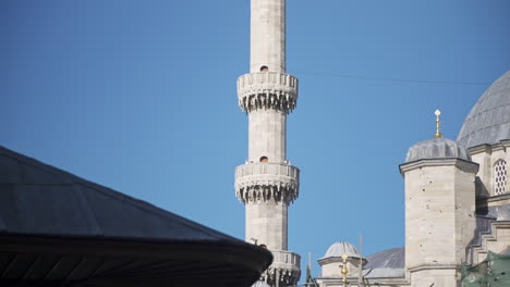 Minarete-De-Mármol-Blanco-De-La-Mezquita-Ese-Lugar-Sagrado-Para-Los-Musulmanes-En-El-Islam,-De-Pie-Frente-Al-Cielo-Azul-Abierto-Mientras-Pájaros-Y-Aviones-Vuelan