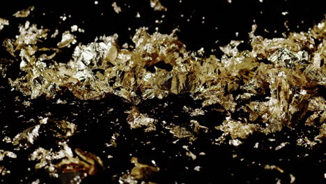 extreme slow motion of gold flakes as two blasts of wind from screen right blow them around on a black background.