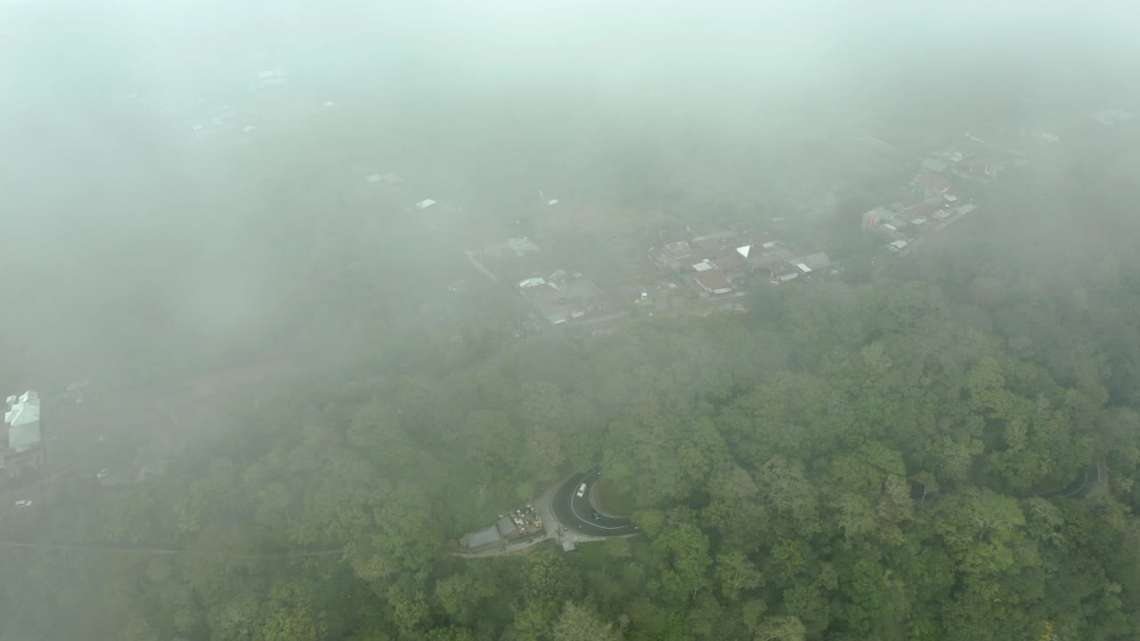 A aerial view with the camera peering down through fog to reveal a lush landscape below