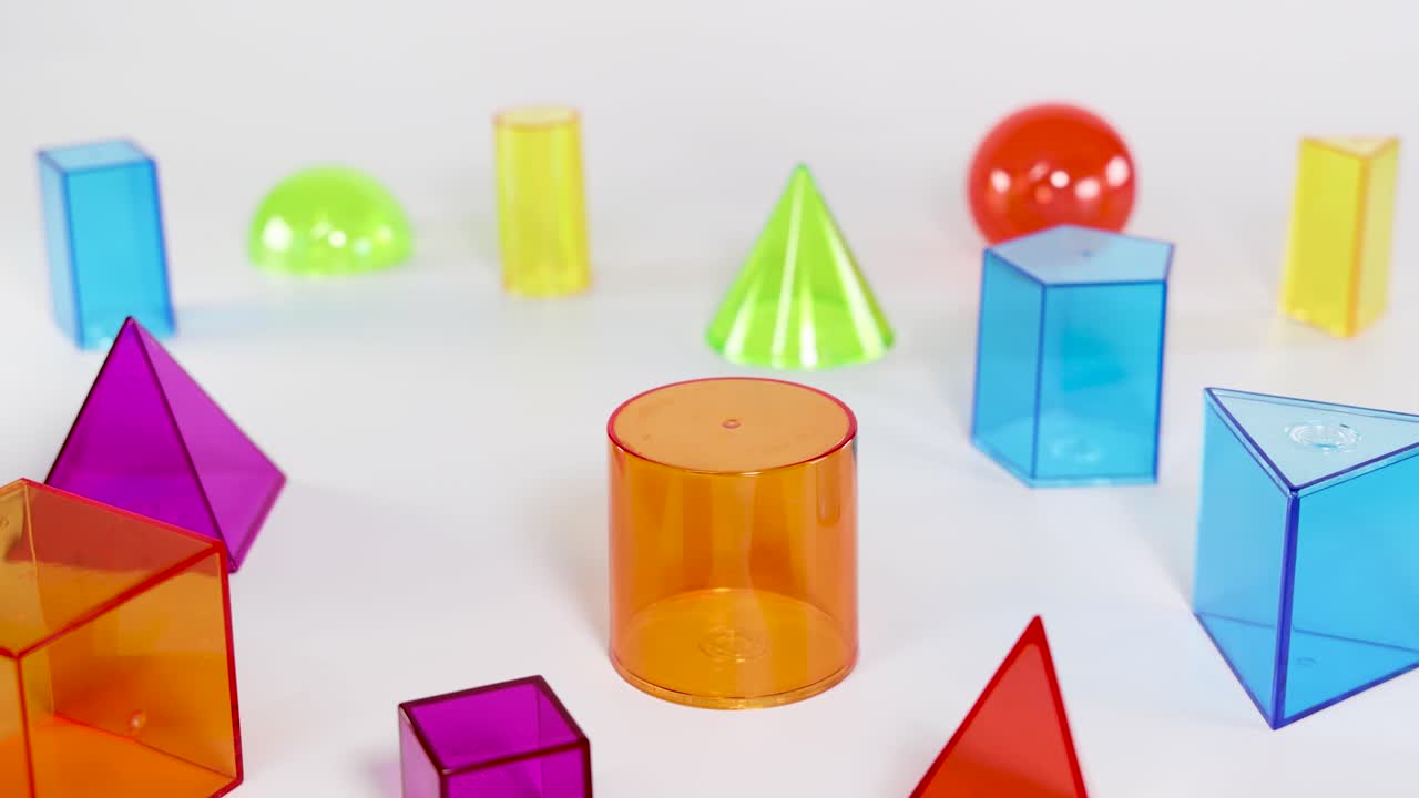 A hand moves an orange cylinder into the center of various colorful geometric solids