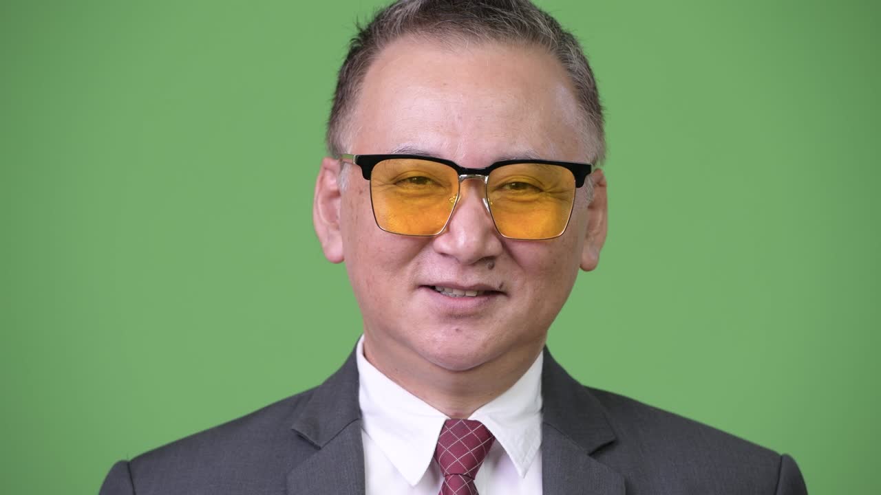 un hombre de negocios japonés maduro con gafas de sol contra un fondo verde.