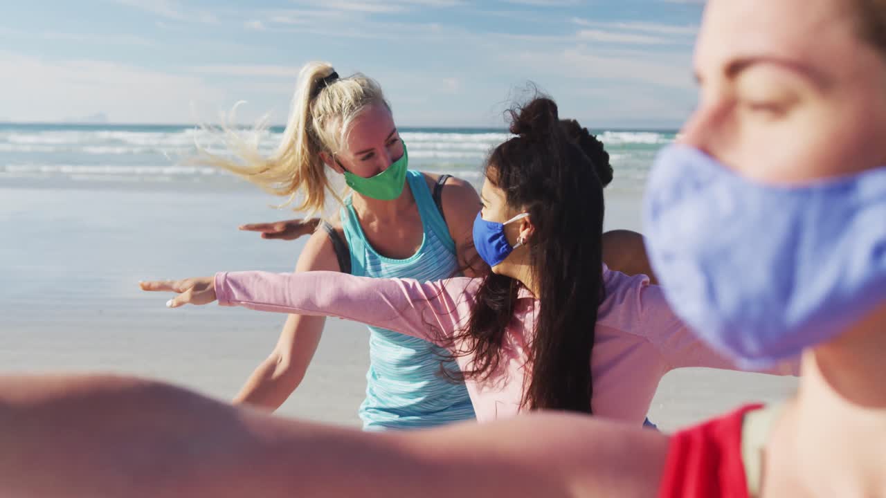 grupo de diversas amigas con máscaras faciales practicando yoga en la playa